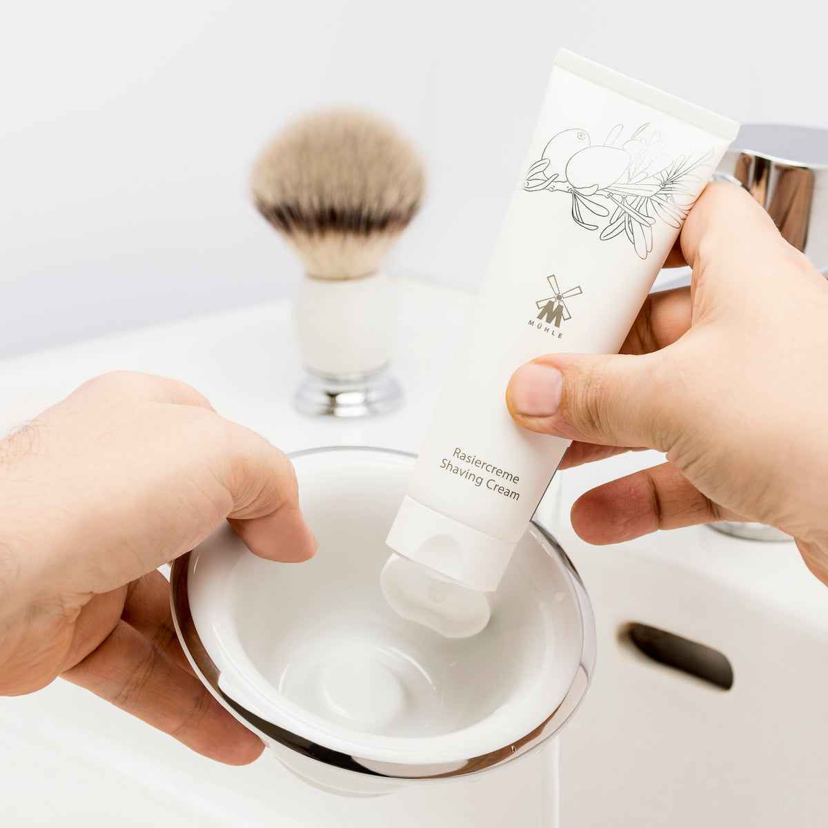 Hånd presser barberskum ud af tube med barbercreme ned i skål – traditionel vådbarbering med luksuriøs barbercreme